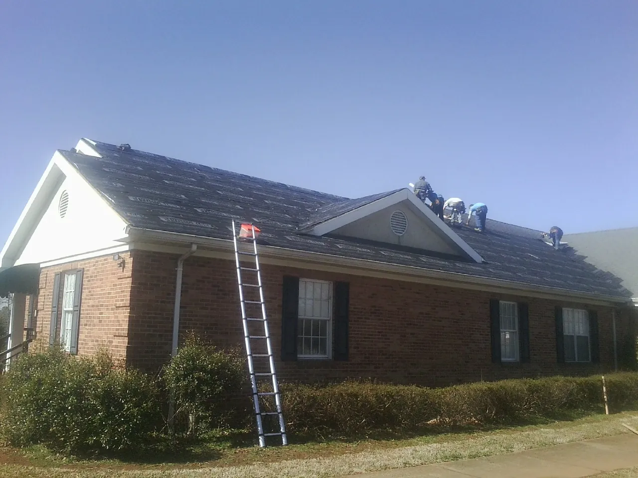 Crew tearing shingles off a brick ranch roof with a ladder set — Metal Roof Repair work by our crew in West Hurley