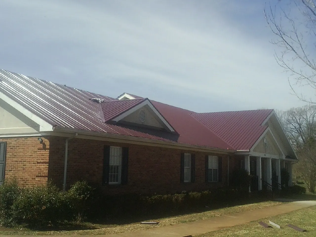 Red metal roof with gabled entries on a long brick building, from a Hail Damage Roof Repair job in West Hurley