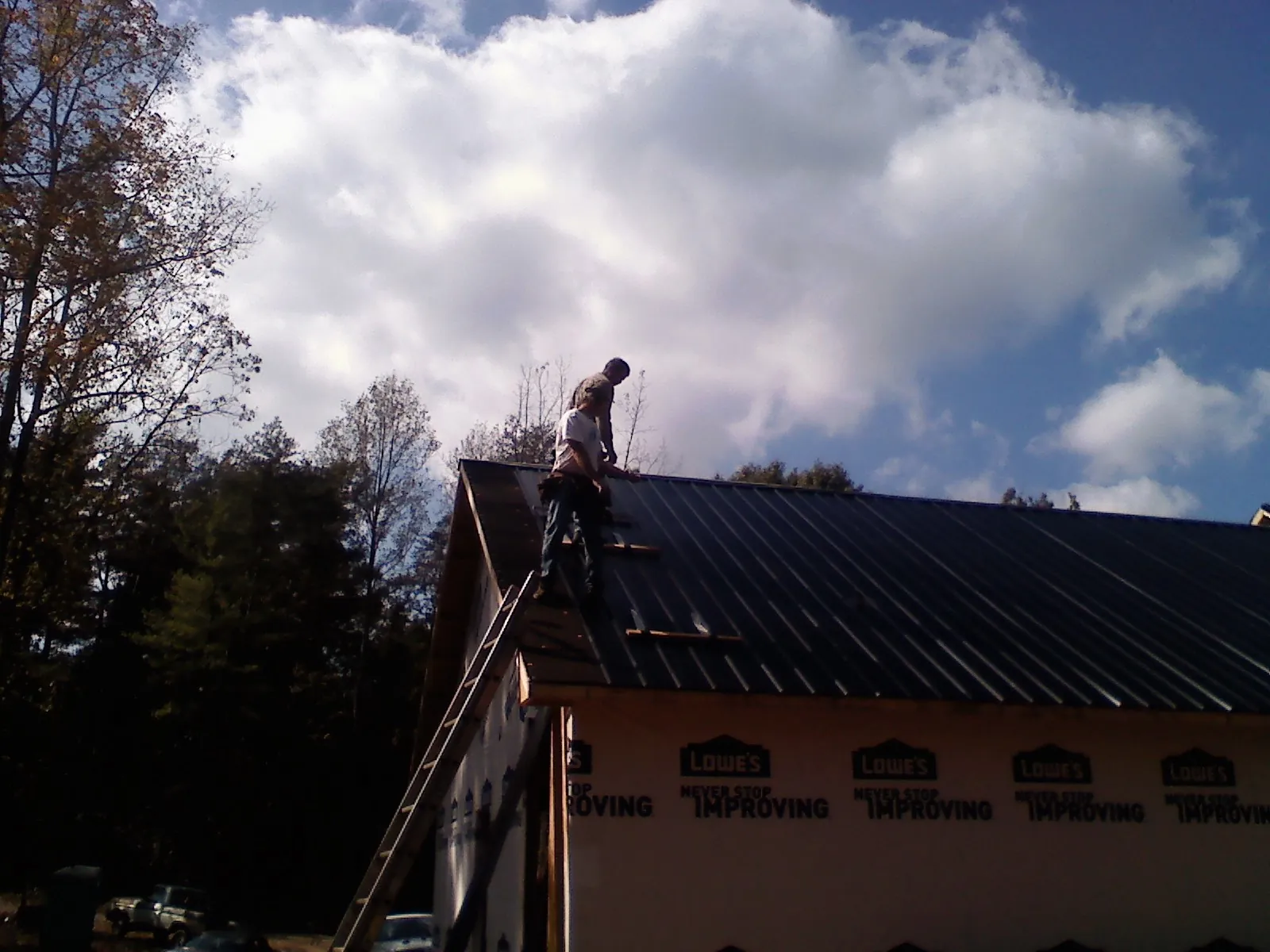 Roofer fastening dark metal panels high against a cloudy sky, from a Roof Inspection job in West Hurley