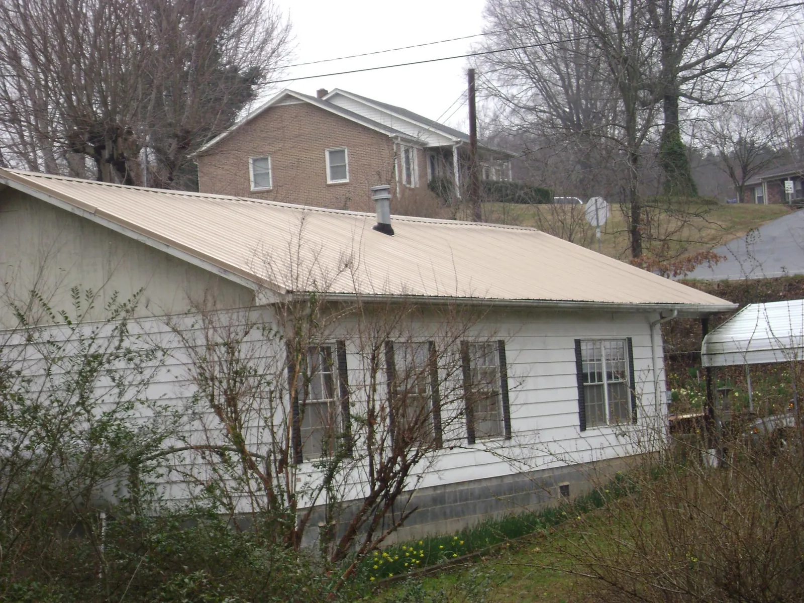 Tan metal roof on a white sided house set into a hillside — Commercial Roofing by Roofing Brothers in West Hurley
